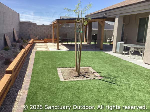Back yard with pet turf, timber border, mesquite tree, mocha paver border, pewter border, pergola over flagstone patio, natural desert grasses, and boulders, with decorative rock