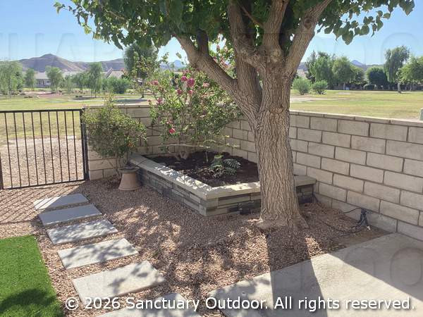 Back yard corner with decorative rock, turf, masonry planter, bird attracting natural plants